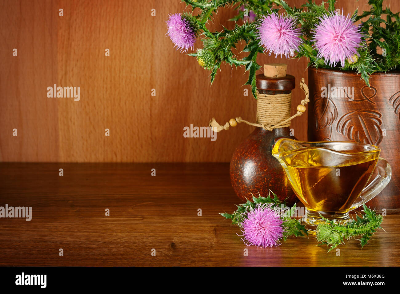 Flowering plant milk thistle and oil glass. Healing herb on wooden background. Free space for text. Stock Photo