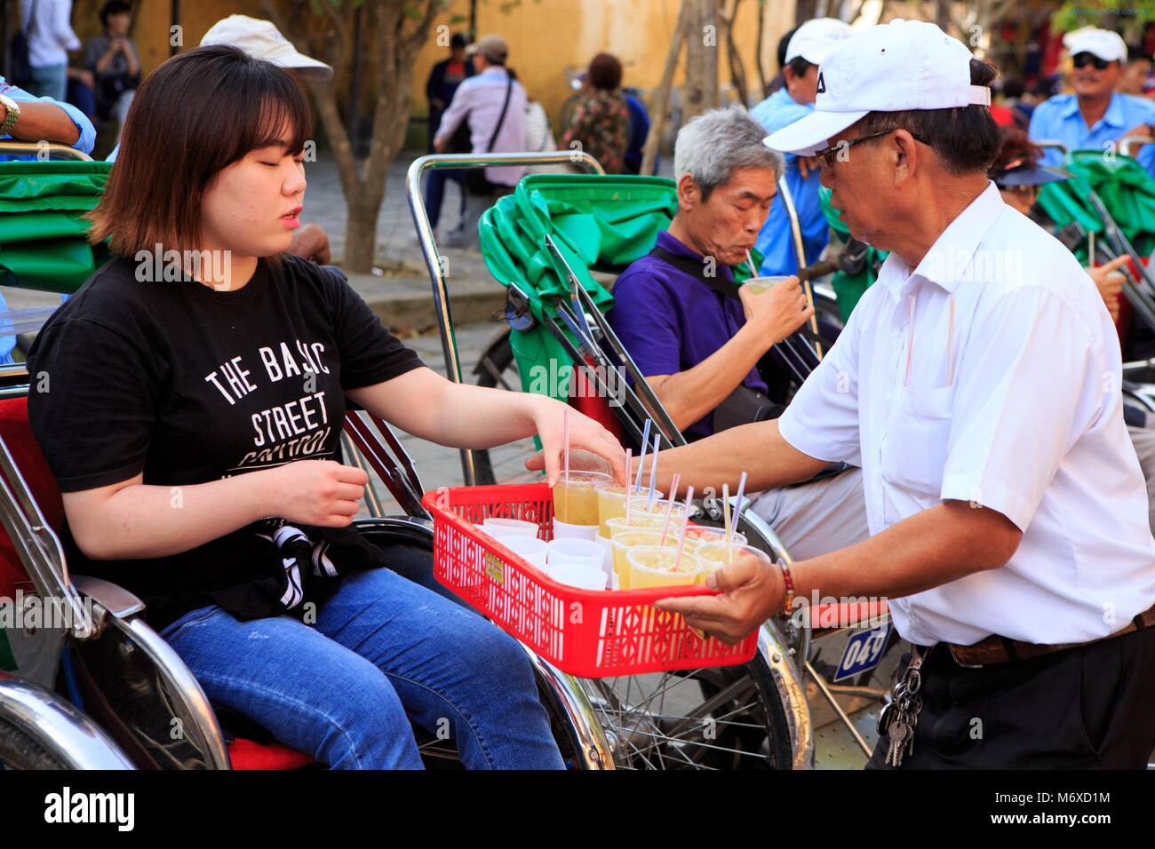 A man gives a tourist a cool drink before a rickshaw ride through the old town of Hoi An Stock Photo