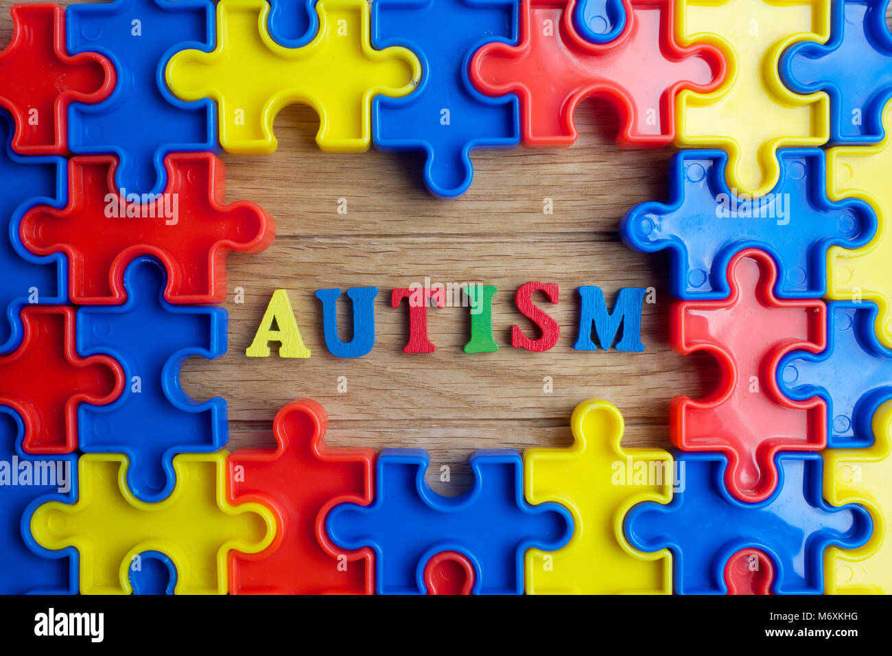Pieces from a colorful jigsaw puzzle arranged to form a page on wooden background. Break barriers together for autism. Stock Photo