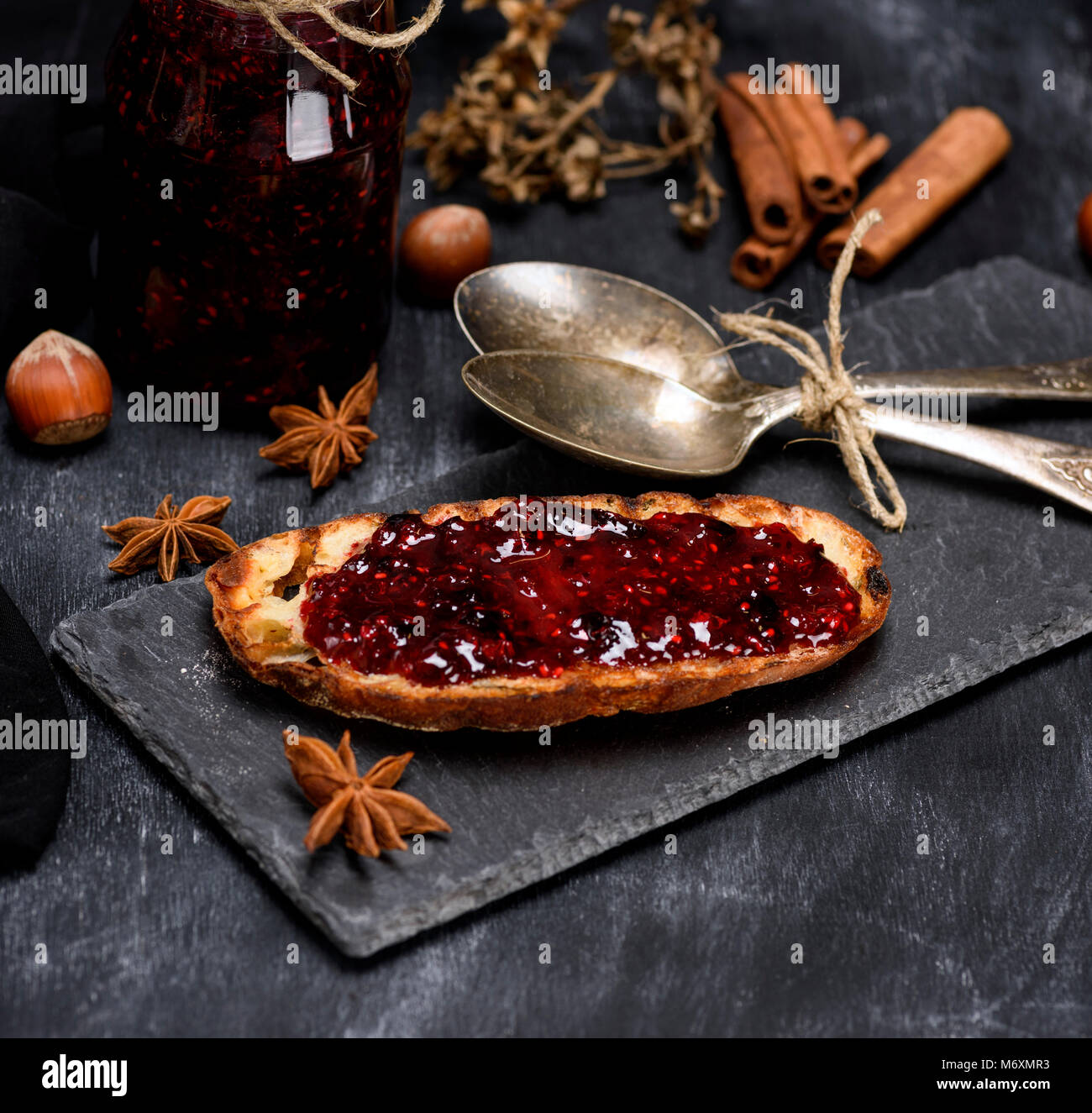 Toast Spoon toast with raspberry jam, two iron spoons and a jar of jam on a black ...