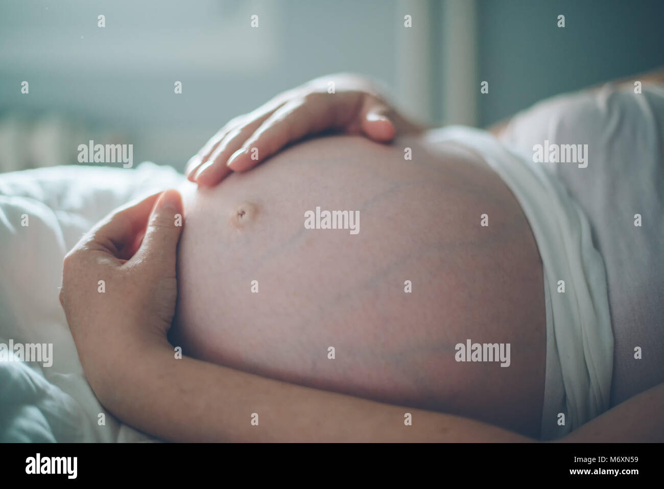 Pregnant woman cuddling belly in bedroom at home just before the labor and childbirth, selective focus Stock Photo