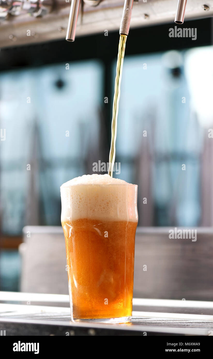 Drafting a glass of chilled draft beer from a tap in a pub in a low angle view of the liquid
