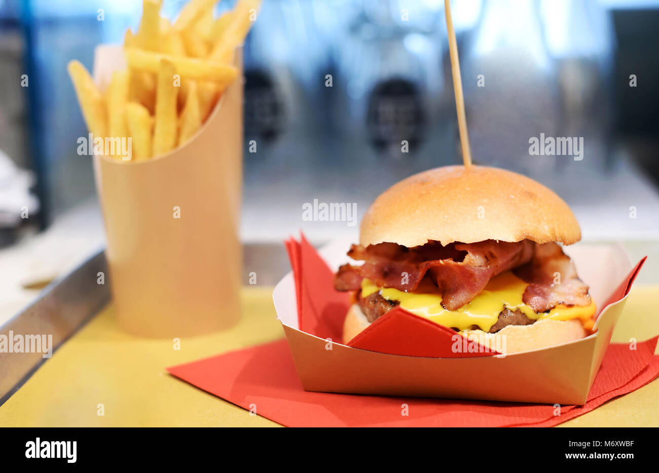 Serving a crunchy hamburger with melted cheese and bacon on a disposable cardboard plate on a tray with a side order of French fries Stock Photo