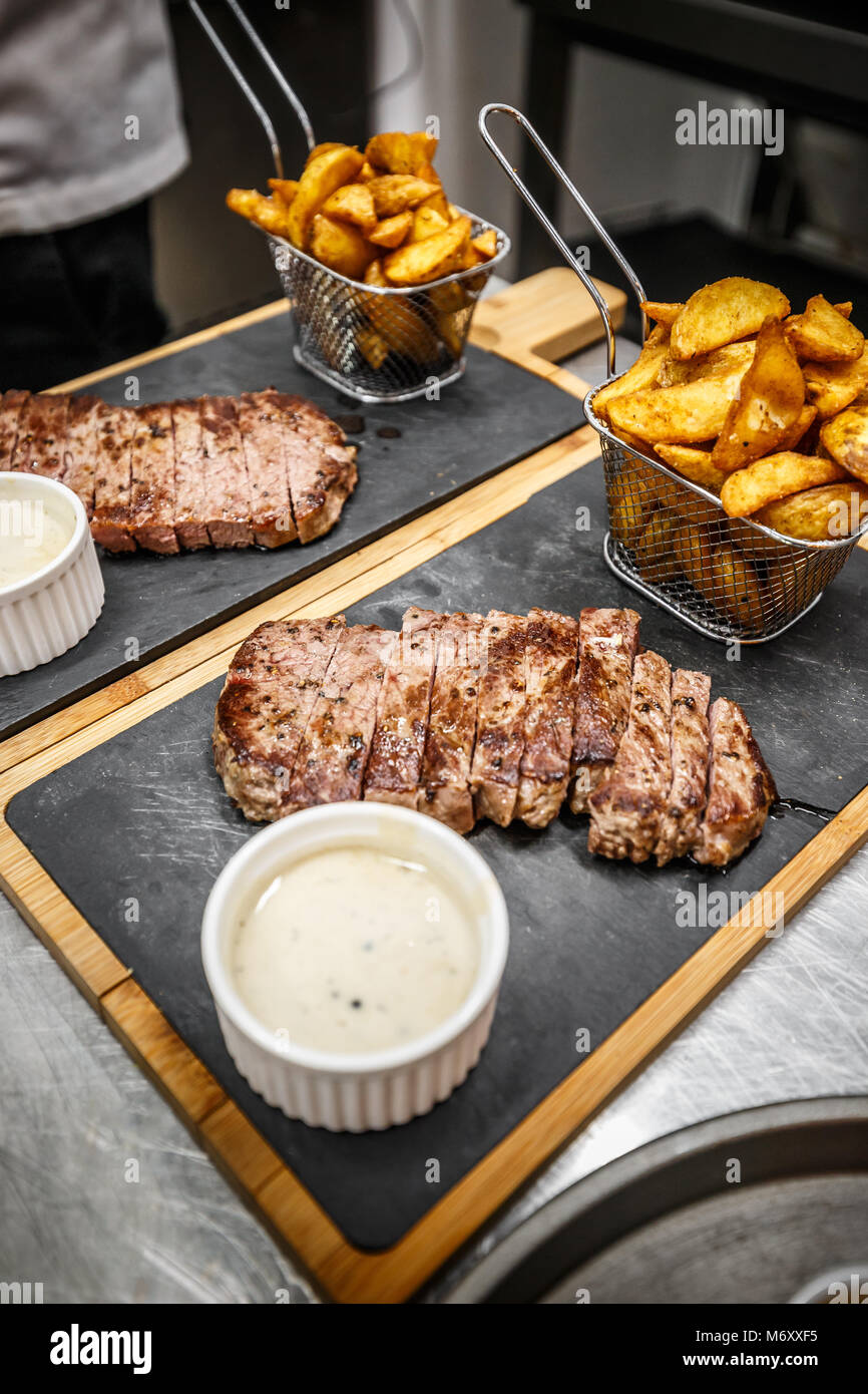 Well done grilled steak with roasted potato wedges on cutting board Stock Photo
