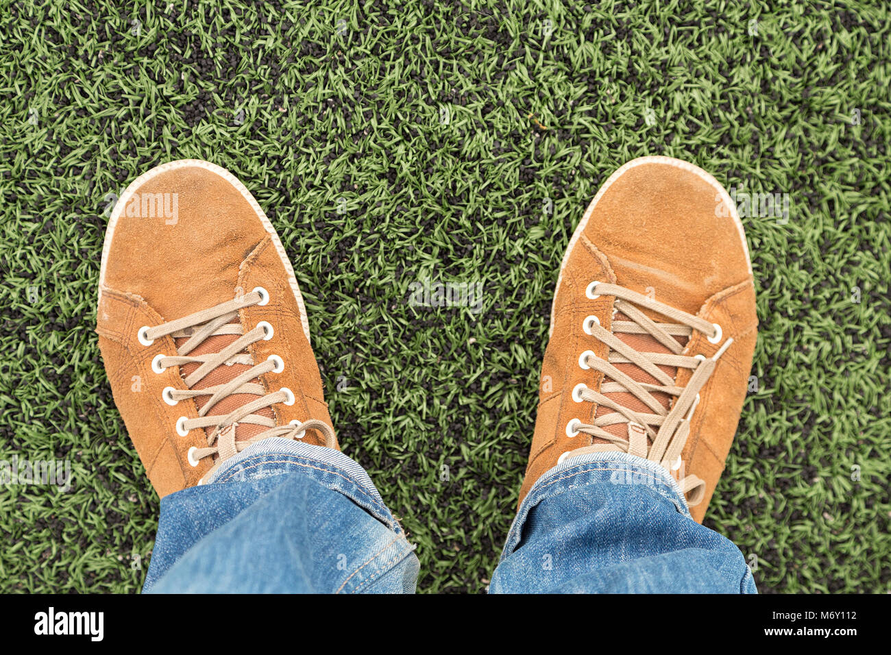 Man in leather orange  sneakers and blue jeans stands on fresh green grass, top view Stock Photo
