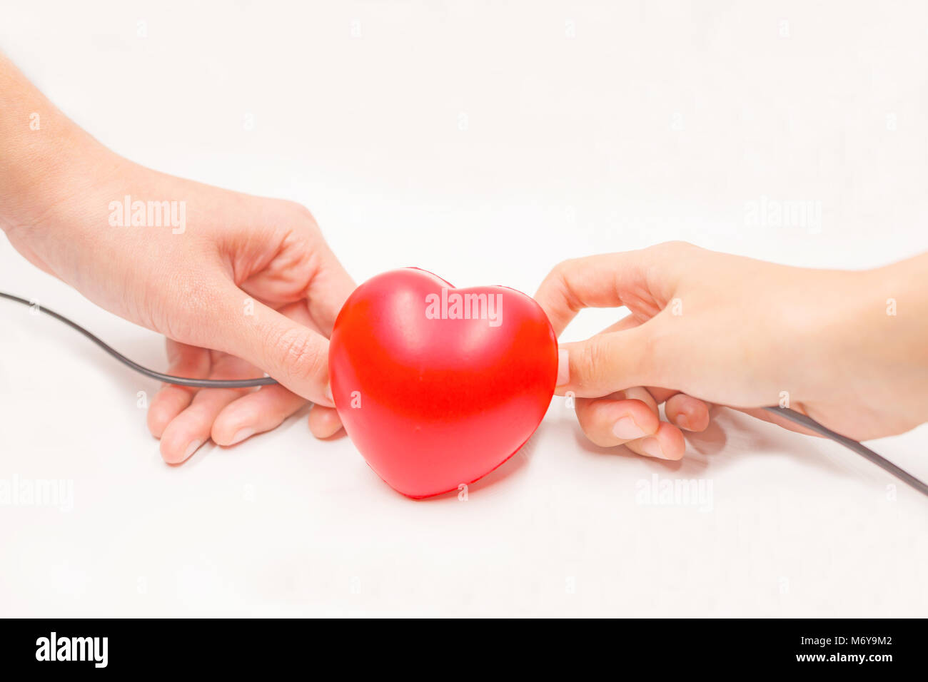 Hands with charging cables to help recovering heart on white background. Heart disease protection, proactive checkup, diagnosis, sickness prevention,  Stock Photo