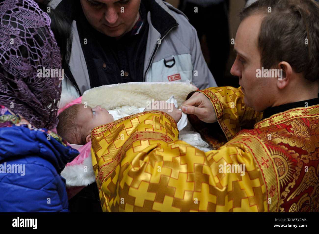 Christening for baby in a rural church. Man and woman holding a baby on hands and a priest standingnear them. January 7, 2018. Bucha village, Ukraine Stock Photo
