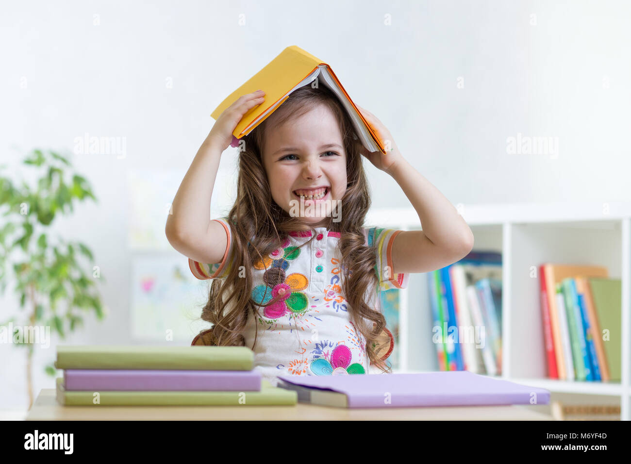 Child girl student in the school holds a book on her head and smiles ...