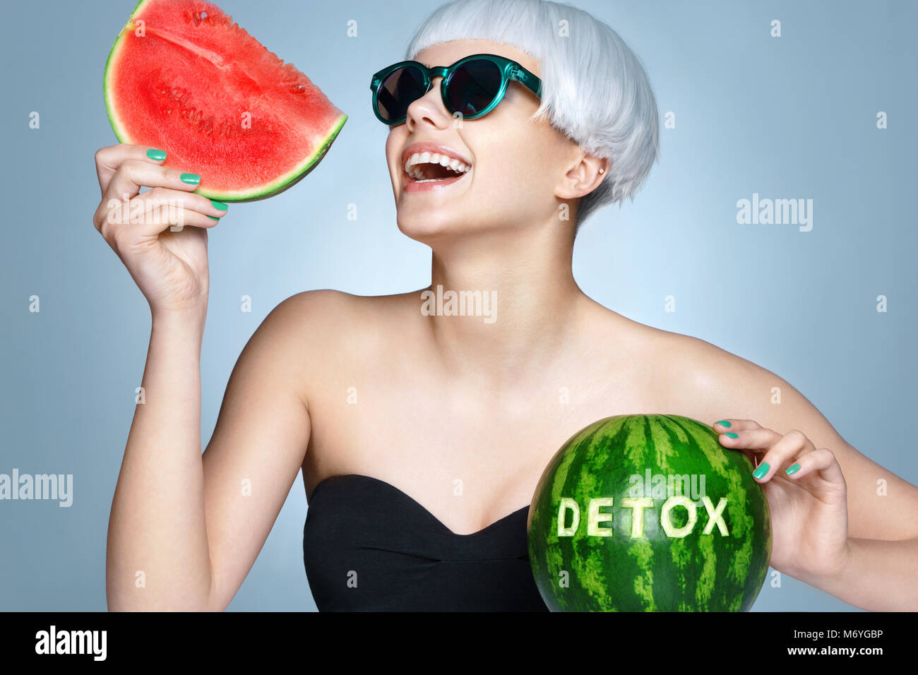 Happy girl with ripe watermelon. Photo of smiling girl in sunglasses on blue background. Detox concept Stock Photo