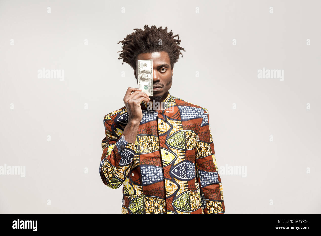 Angry african man holding one dollar. Indoor, isolated on gray background Stock Photo