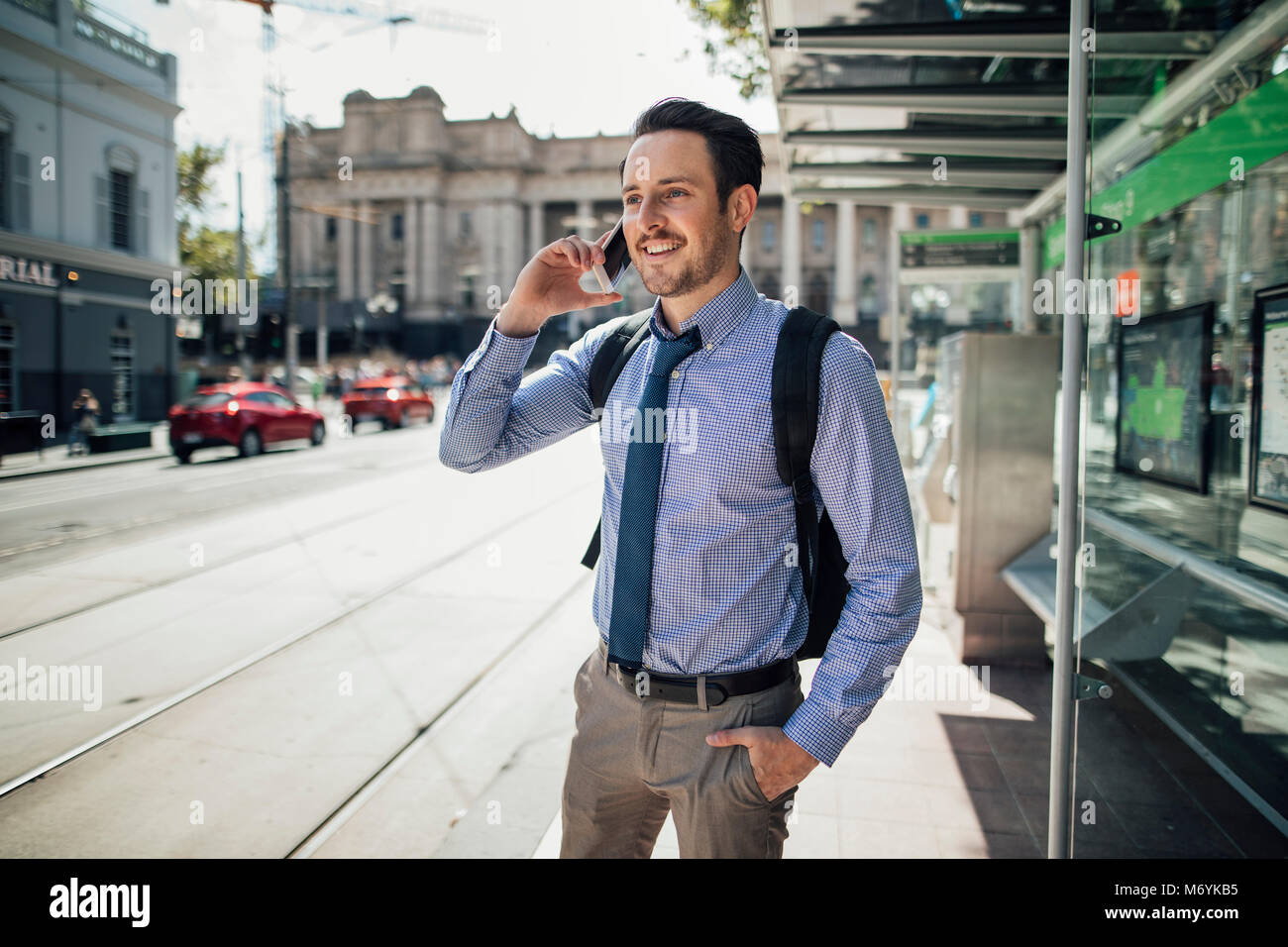 Millennial businessman is talking on his smartphone while waiting for a tram in Melbourne, Victoria. Stock Photo