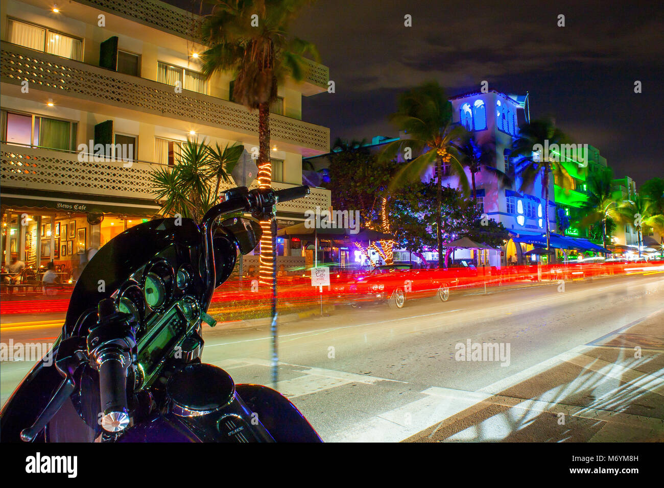 Ocean Drive in Miami at night with vibrant street colours. Cars passing by creating lines of light during long exposure. Bike in foreground. Stock Photo