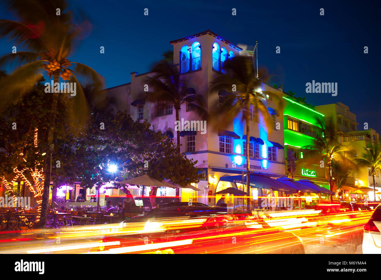 Ocean Drive in Miami at night with vibrant street colours. Cars passing by creating lines of light during long exposure. Palms, hotel in background. Stock Photo