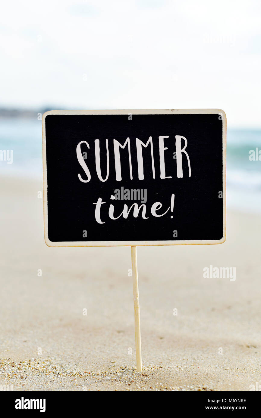 closeup of a black signboard with the text summer time written in it, on the sand of a quiet beach Stock Photo