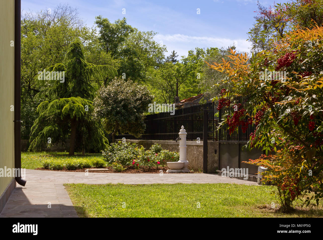 View of a house garden with a white fountain and a sliding gate Stock Photo