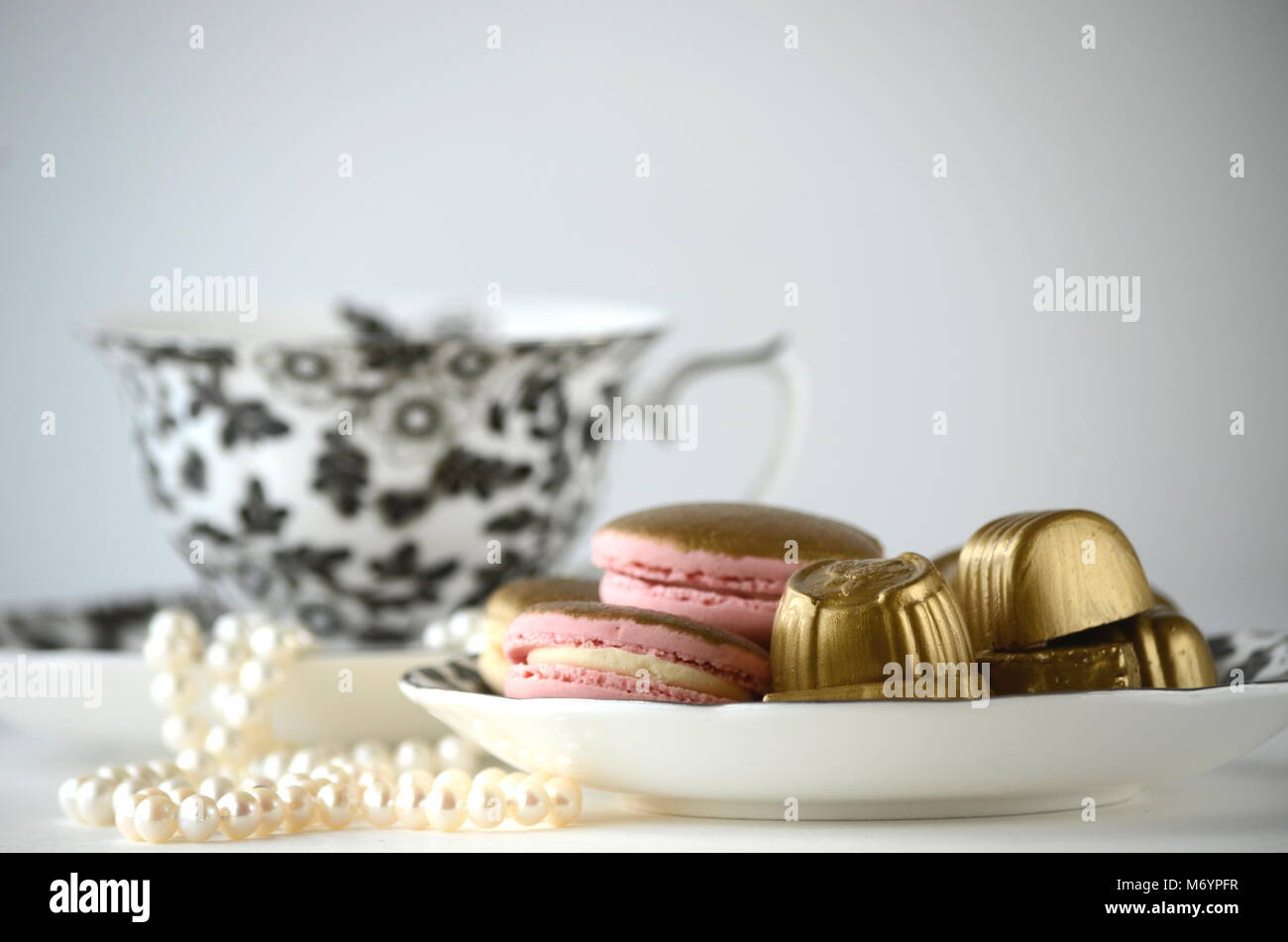 Gold and pink French macarons, chocolates with a black and white cup of