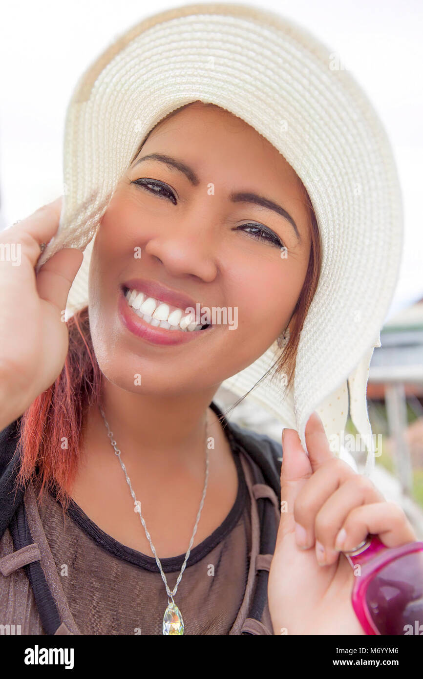 Beautiful Filipino woman modeling a wide-brim white hat. She has clear complexion, wide toothy smile and is wearing makeup. Stock Photo