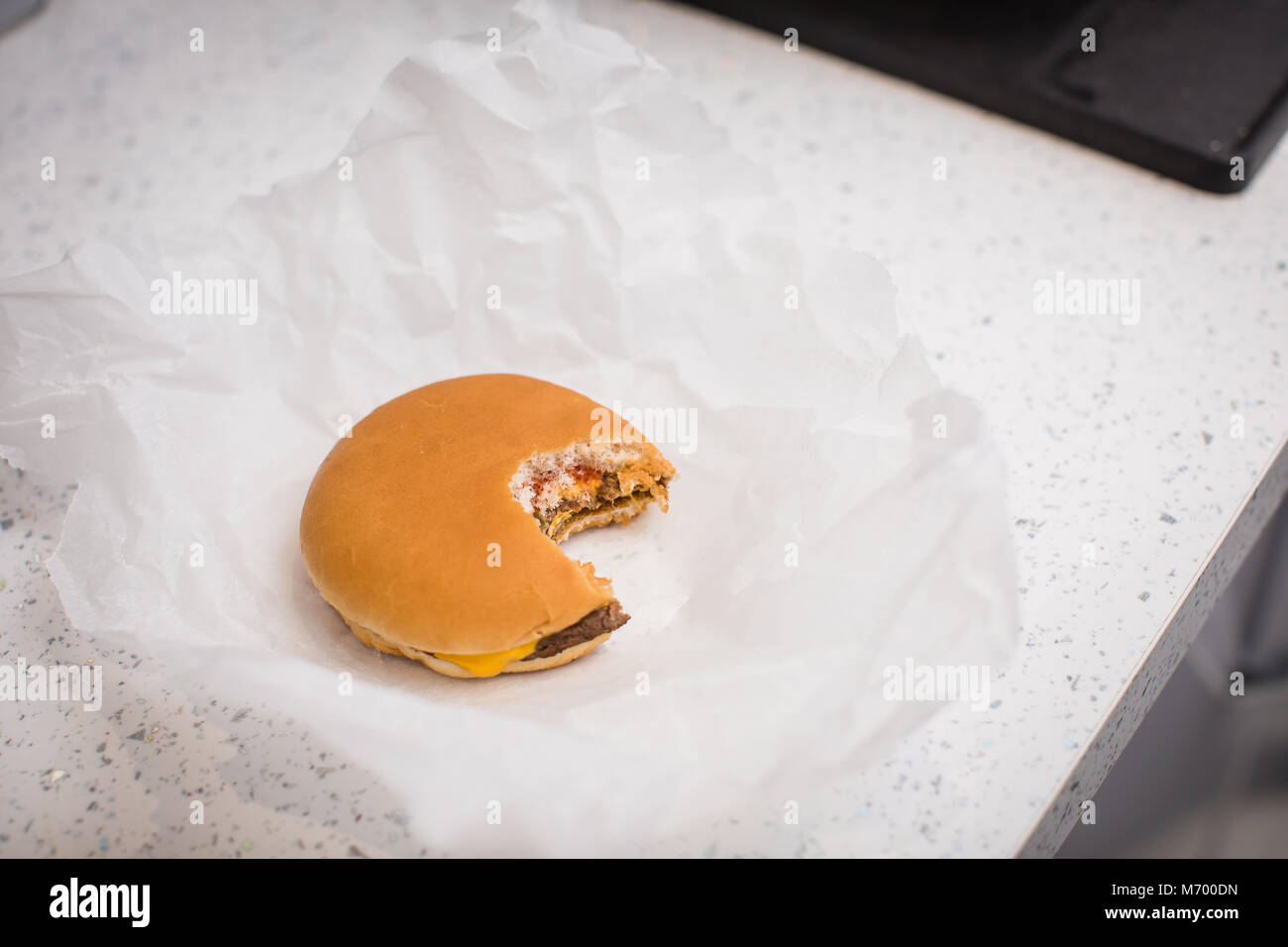 Single cheese burger with a bite taken out of it sat on a table top in a  grease proof paper wrapper Stock Photo - Alamy