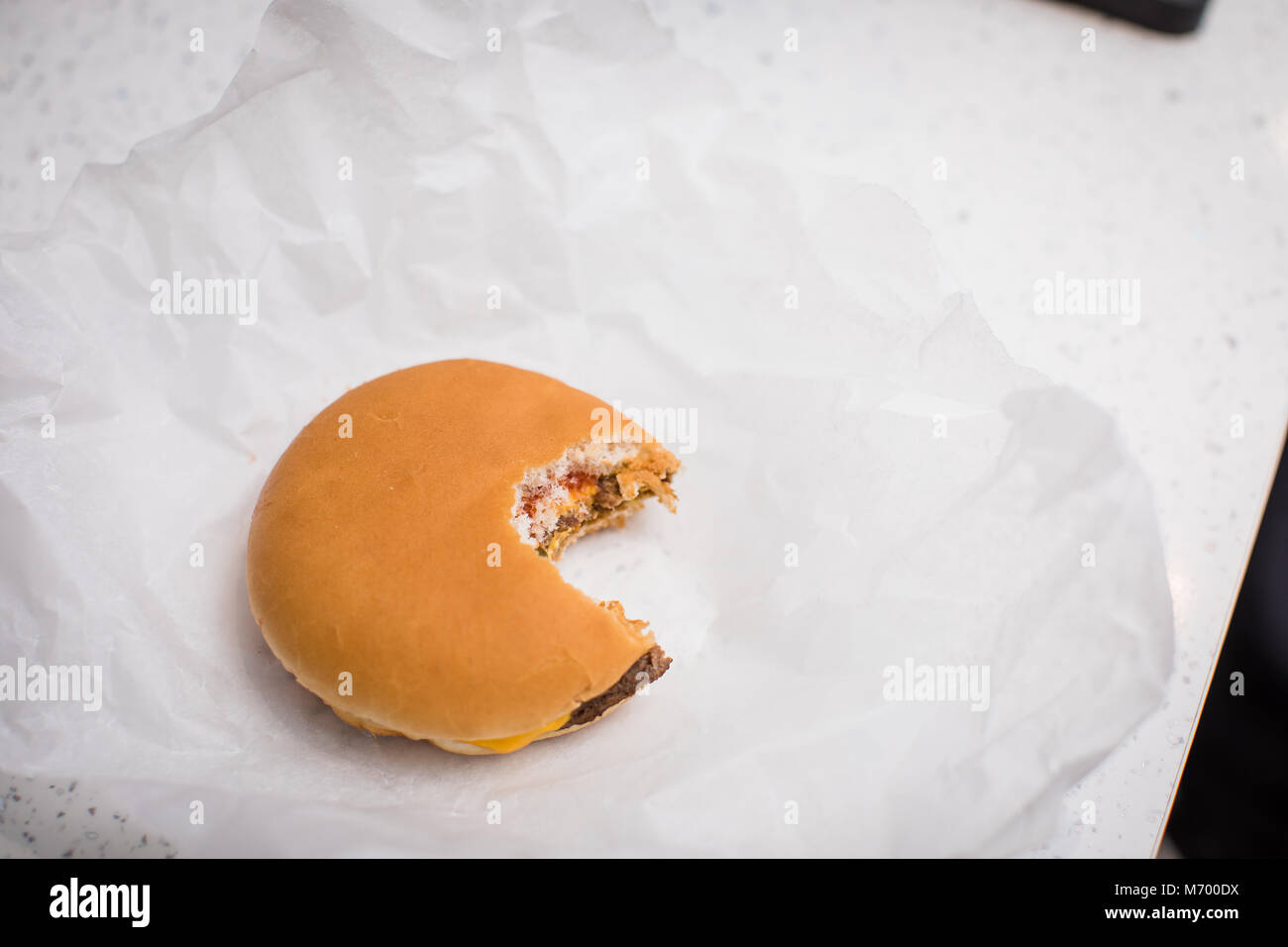 Single cheese burger with a bite taken out of it sat on a table top in