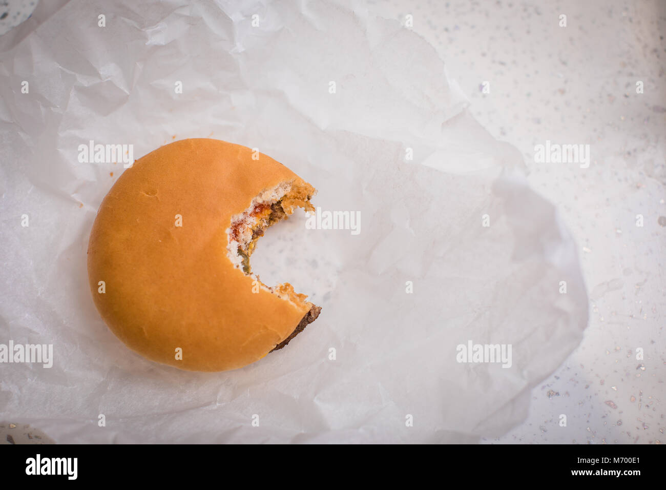 Single cheese burger with a bite taken out of it sat on a table top in