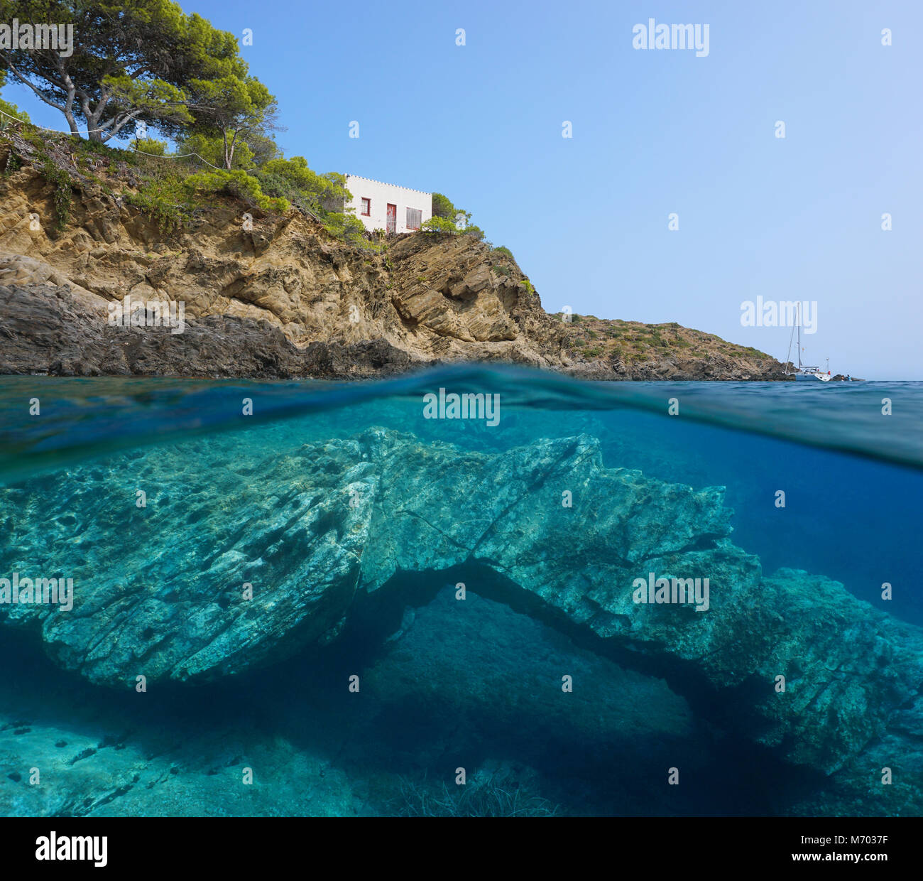 Rocky coast with a small house and a natural rock formation underwater in the Mediterranean sea, split view above and below water surface, Spain Stock Photo