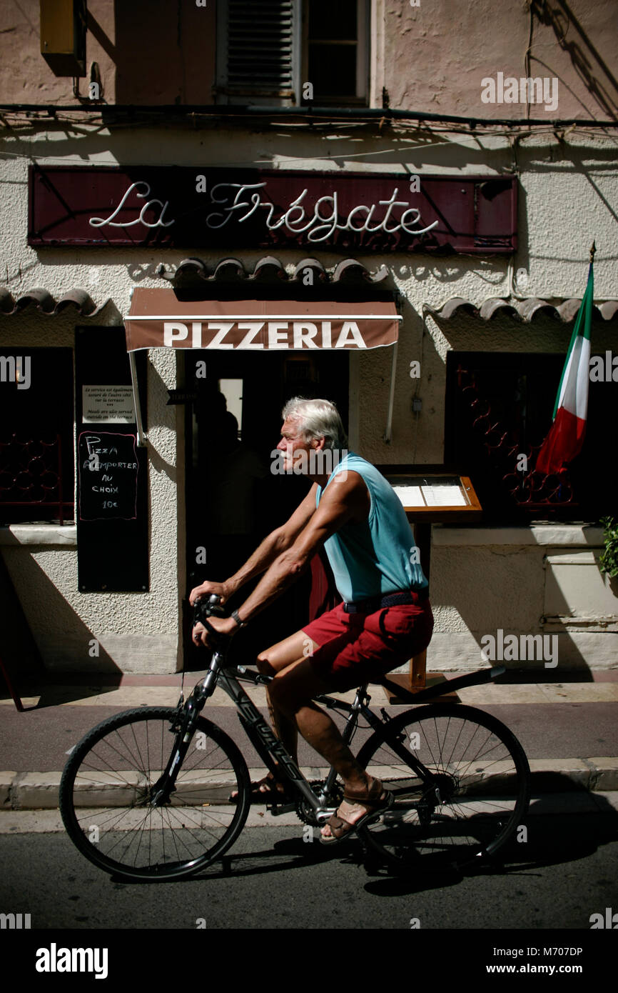 Man rides bike on a street through the village of Saint Tropez, France