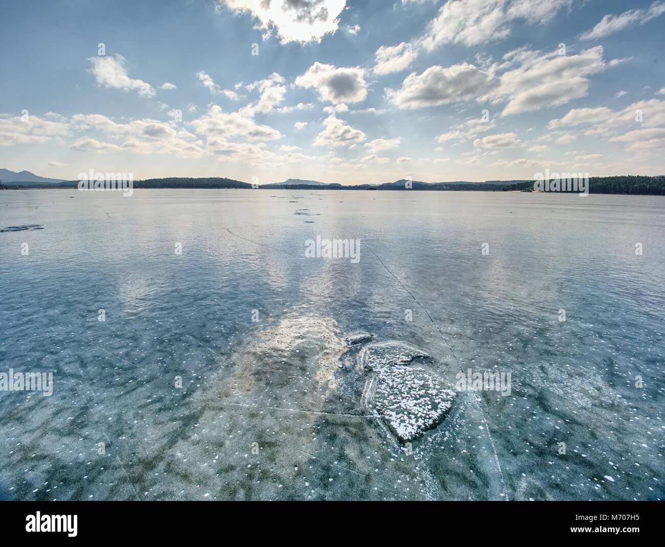 Ice shards on a frozen lake. The rays of the sun creat rainbow shadows in the cracks of the ice. Stock Photo