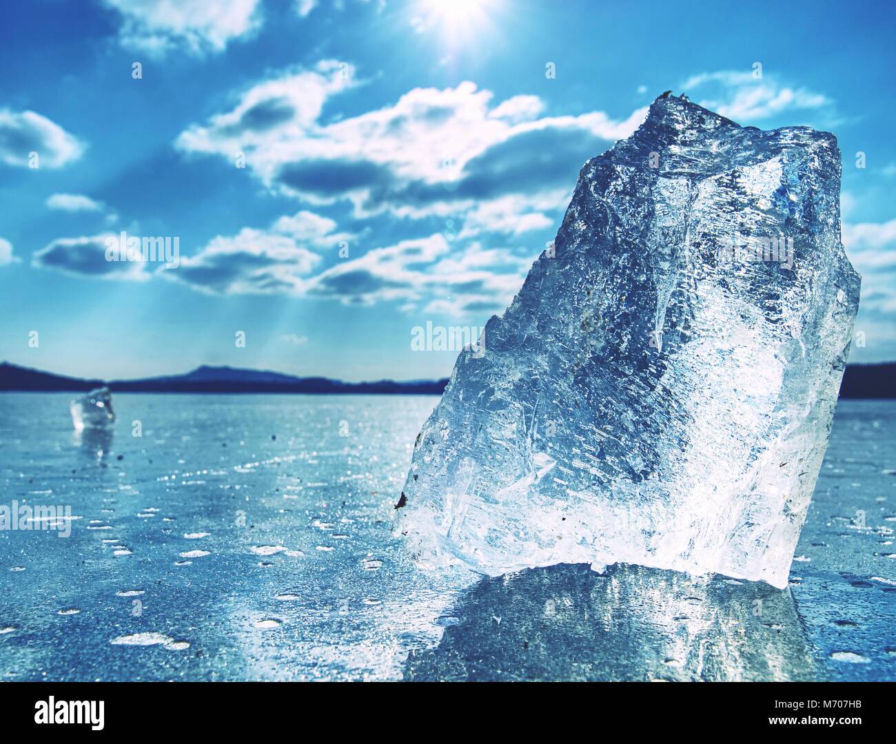 Ice shards on a frozen lake. The rays of the sun creat rainbow shadows in the cracks of the ice. Stock Photo