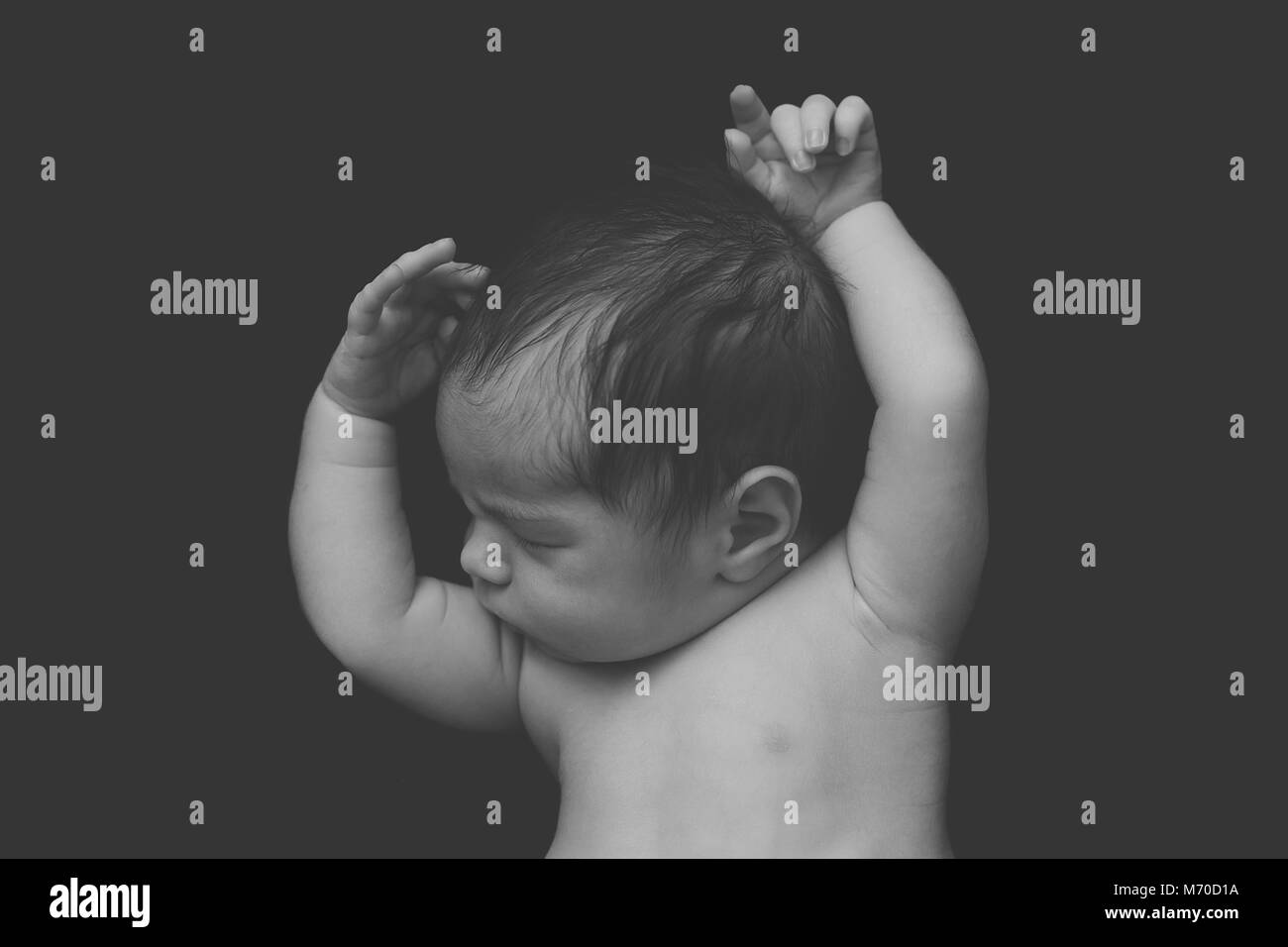 newborn baby boy asleep holding up his hands on a black background, black and white photo Stock Photo