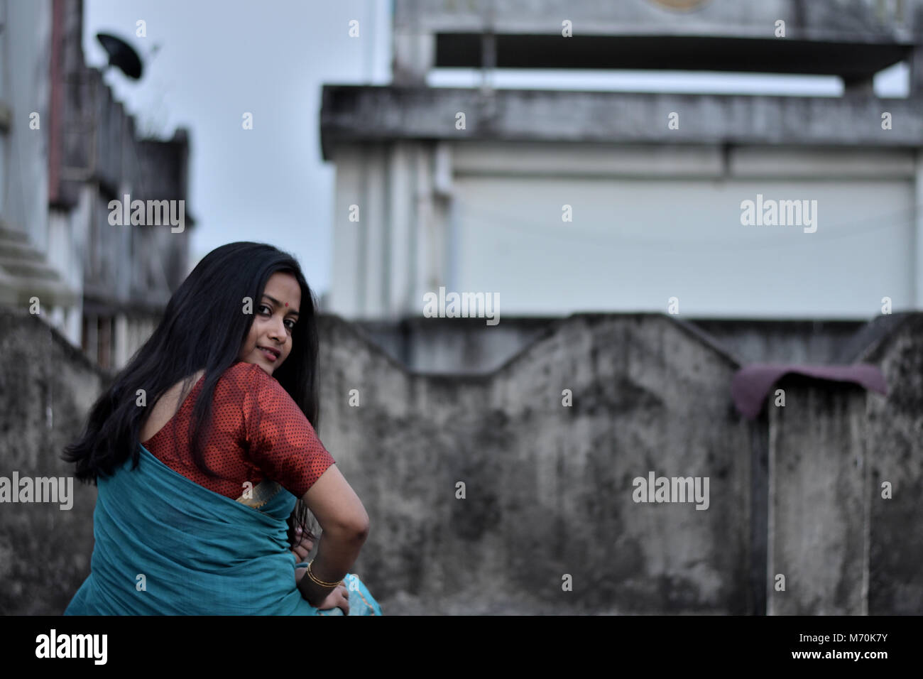 Beautiful Bengali Girl turning her head to look back while sitting on rooftop Stock Photo