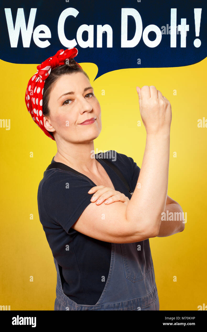 Self-confident middle aged woman with dungarees flexing her muscles, speech bubble with text WE CAN DO IT, tribute to american icon Rosie Riveter Stock Photo