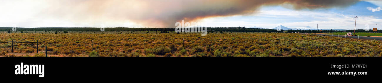 Three Sisters are barely viewable behind a large billowing smoke cloud rising from a summer wildfire Stock Photo