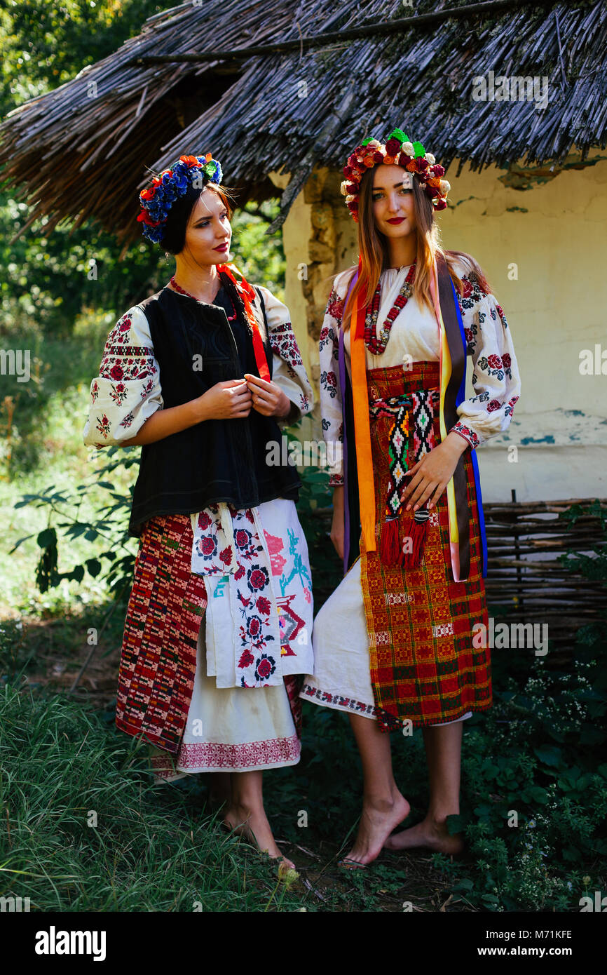 two Beautiful Ukrainian girl  blond and brunette in national embroidered clothes on a background of a wooden hut in summer Stock Photo