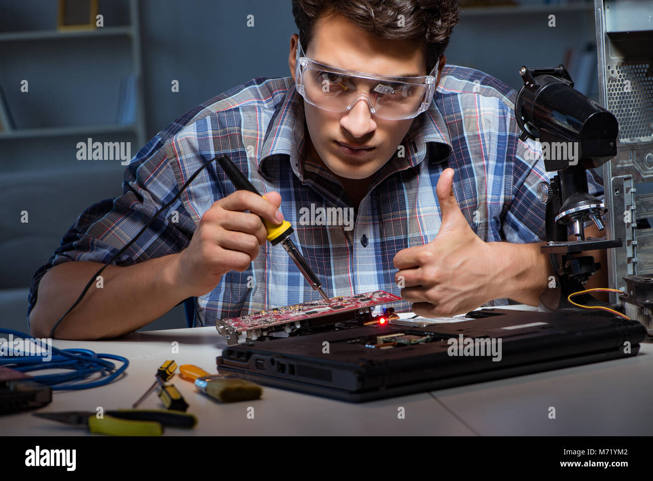 Young repair technician soldering electrical parts on motherboard Stock