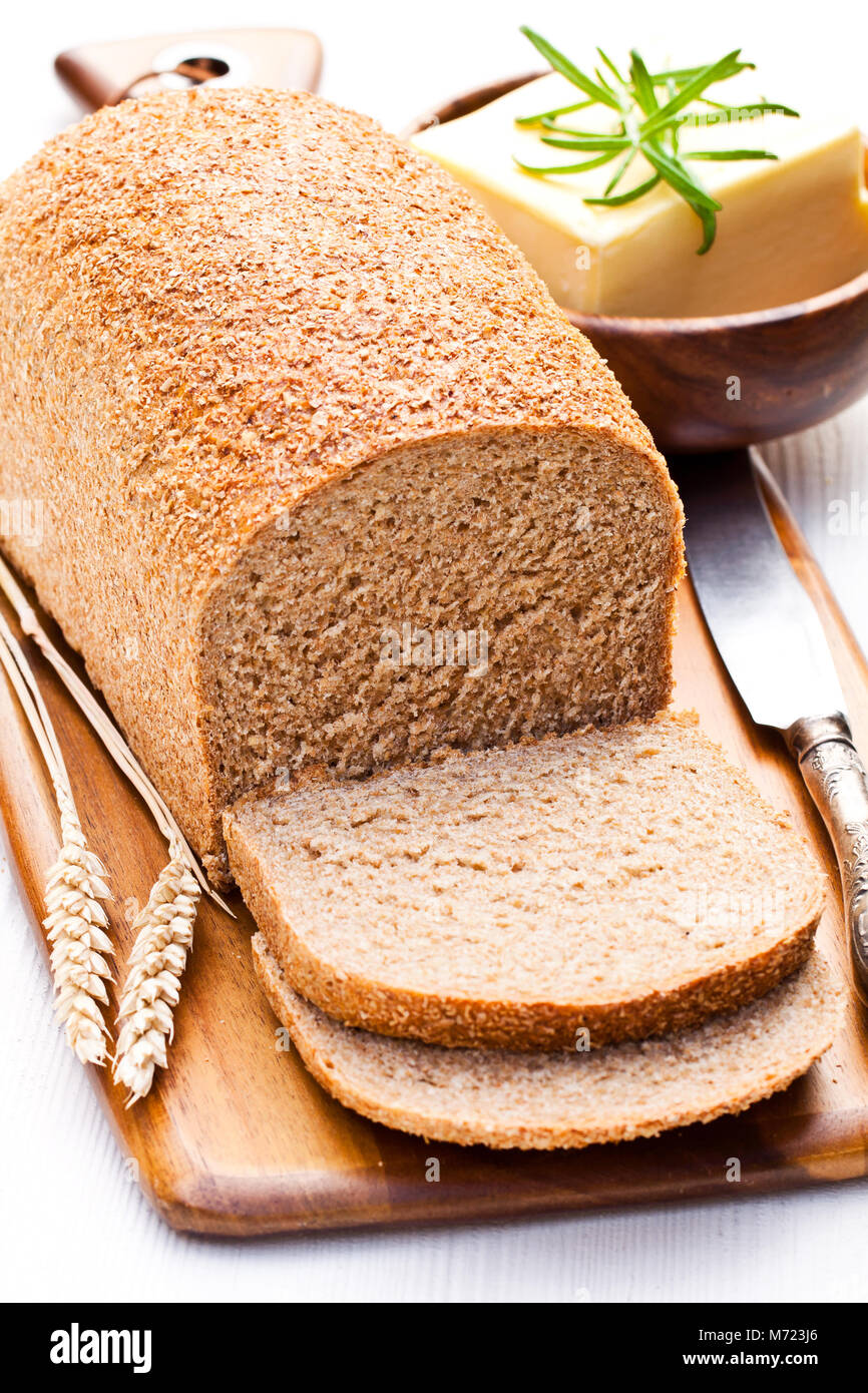 Sliced  slow-baked organic wholemeal bread with butter and rosemary and wheat ears Stock Photo