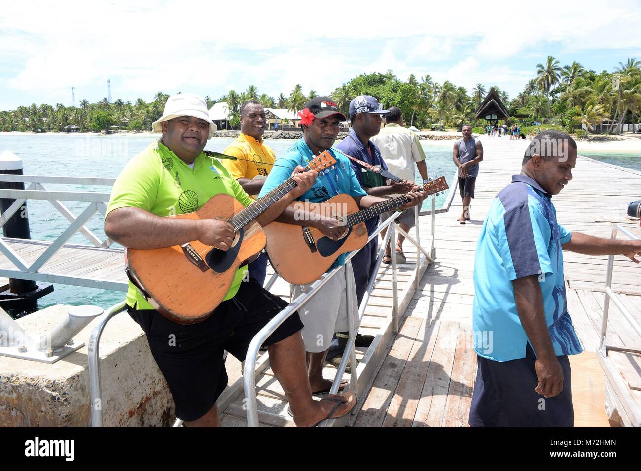 A band of Fijian singers welcome tourists on the beach when they arrive by boat to a beautiful island. They sing traditional Fijian welcome songs. Stock Photo