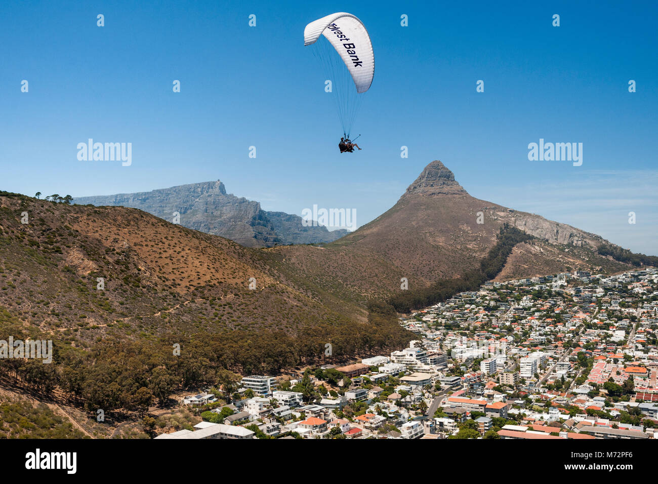Tandem paraglider flying above Cape Town’s Atlantic seaboard suburb of Fresnaye with Table Mountain and Lion’s Head in the background. Stock Photo