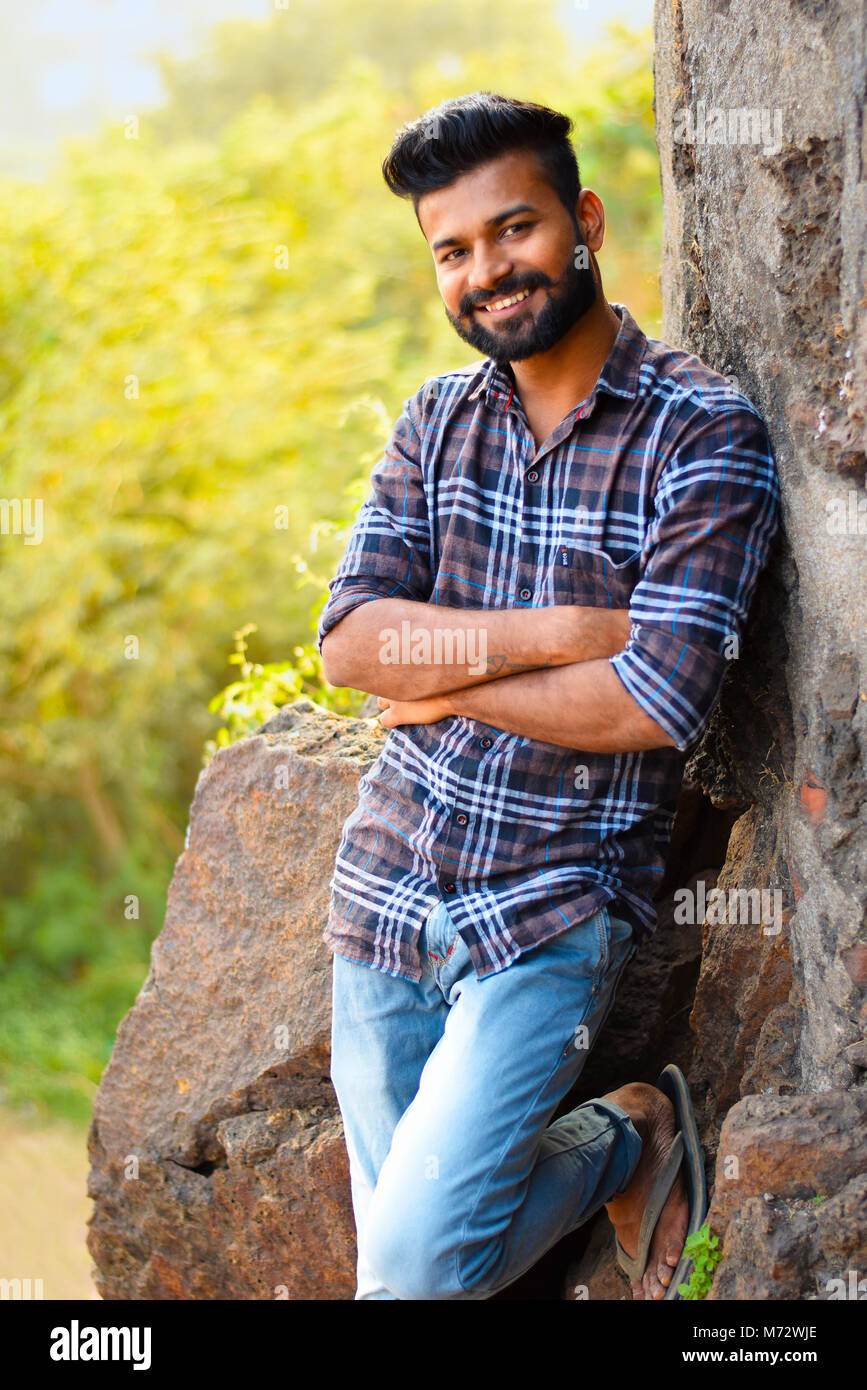 Male model smiling at camera resting on rock. Mumbai, Maharashtra Stock Photo
