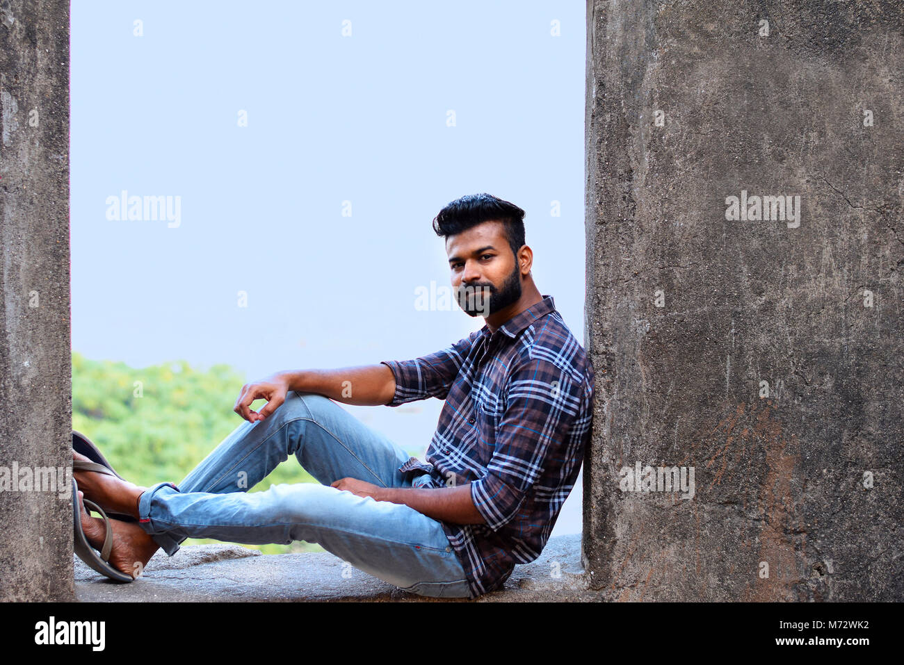 Male model sitting on a rock ledge looking at camera, Sion fort, Mumbai, Maharashtra Stock Photo