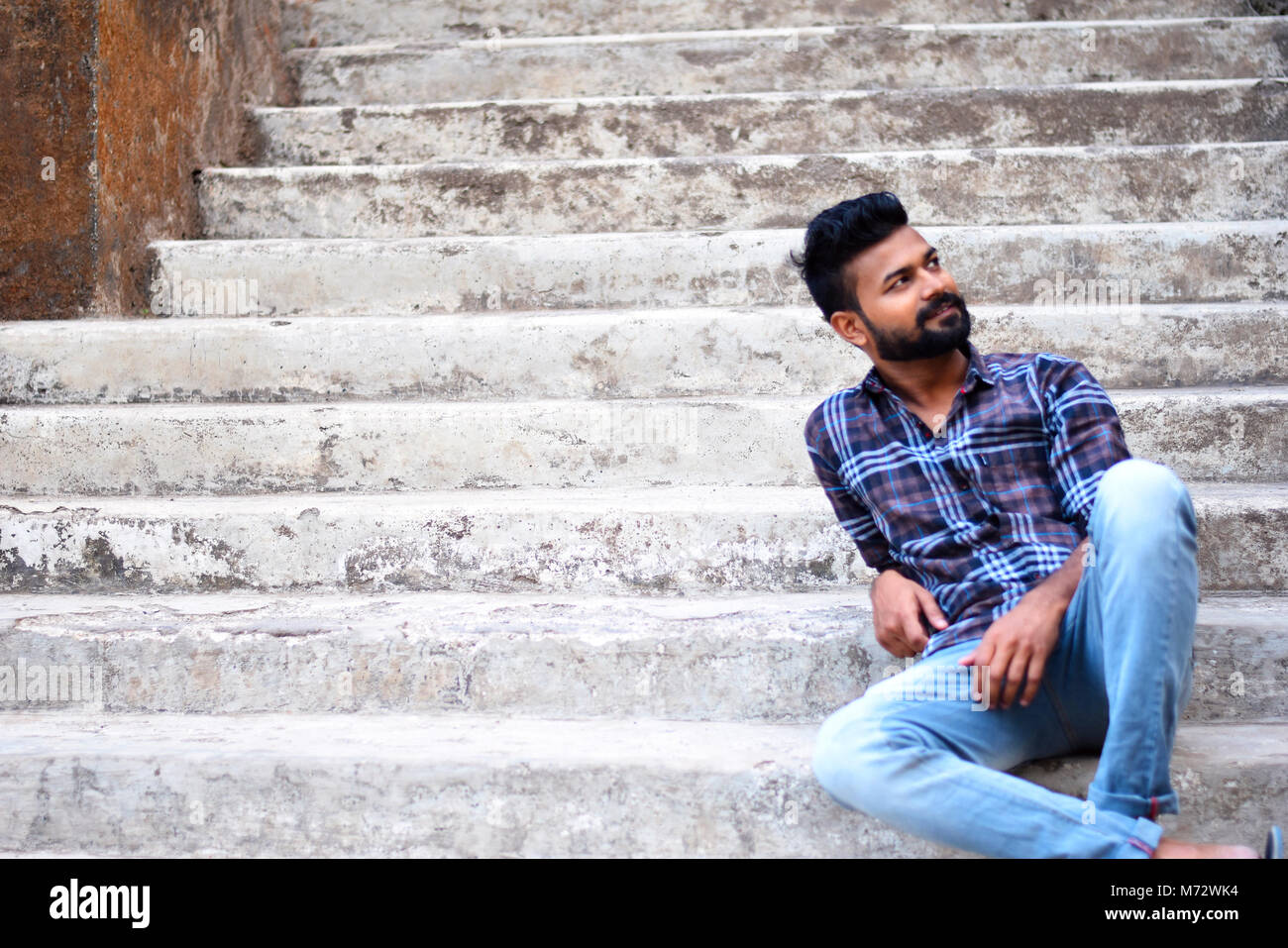 Male model sitting stairs looking up Sion fort, Mumbai, Maharashtra Stock Photo