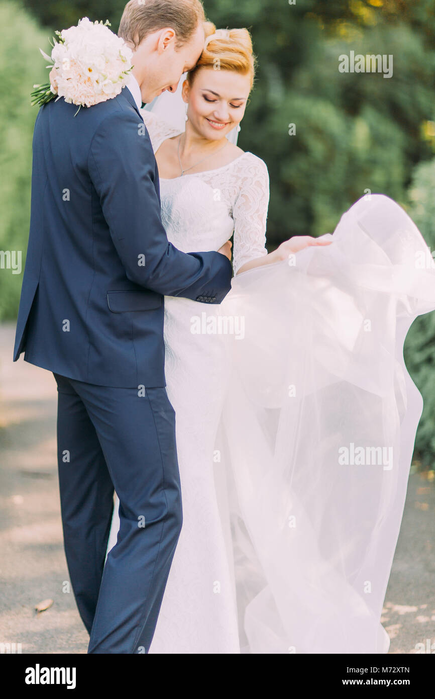 Happy young gentle groom and bride posing at the park. Bridal wedding bouquet of flowers in hands Stock Photo