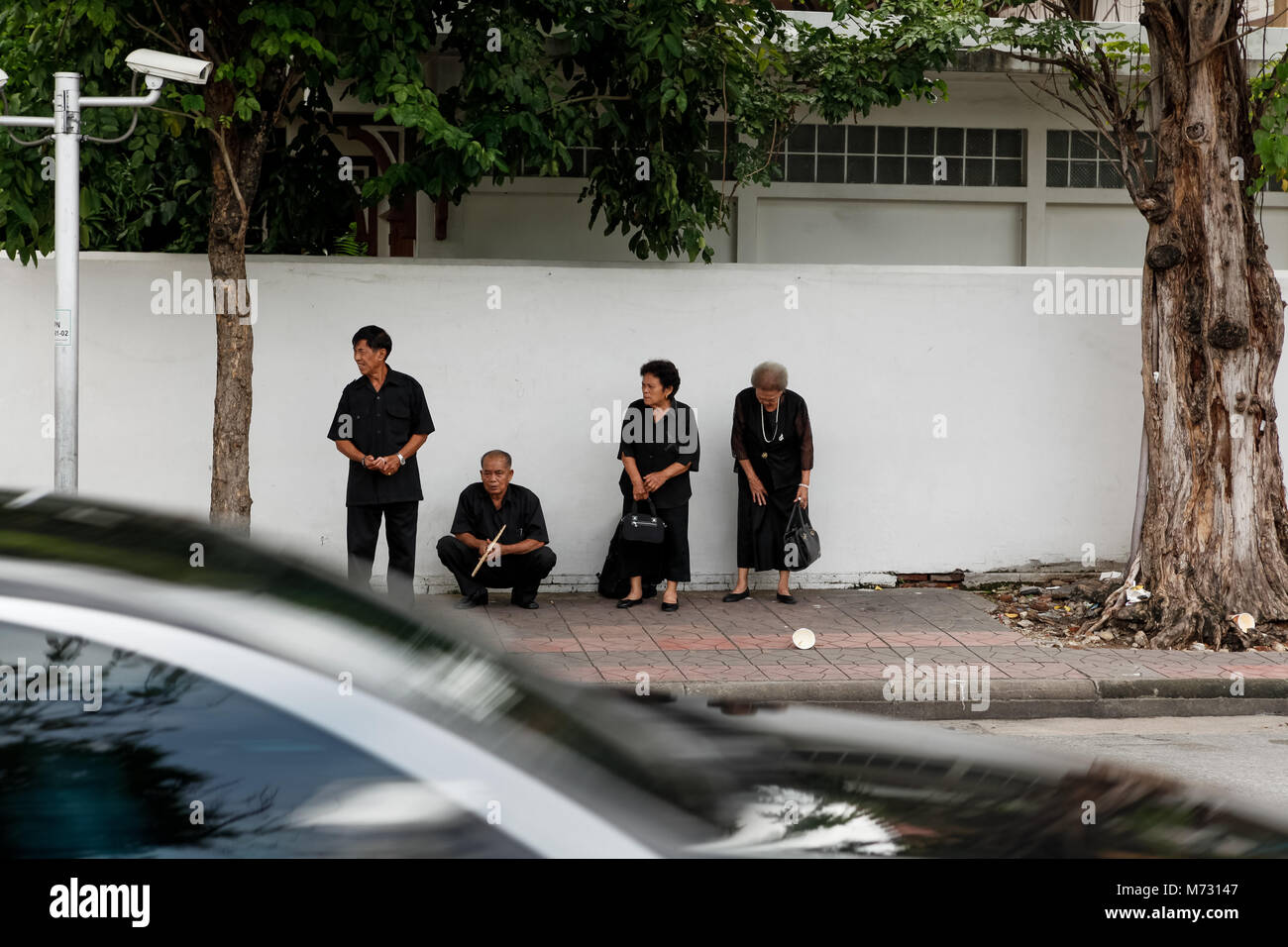 Four people in black clothes, standing on the sidewalk of the street in Ratchadamnoen Road during the mourning for the late Thai king Bhumibol Stock Photo