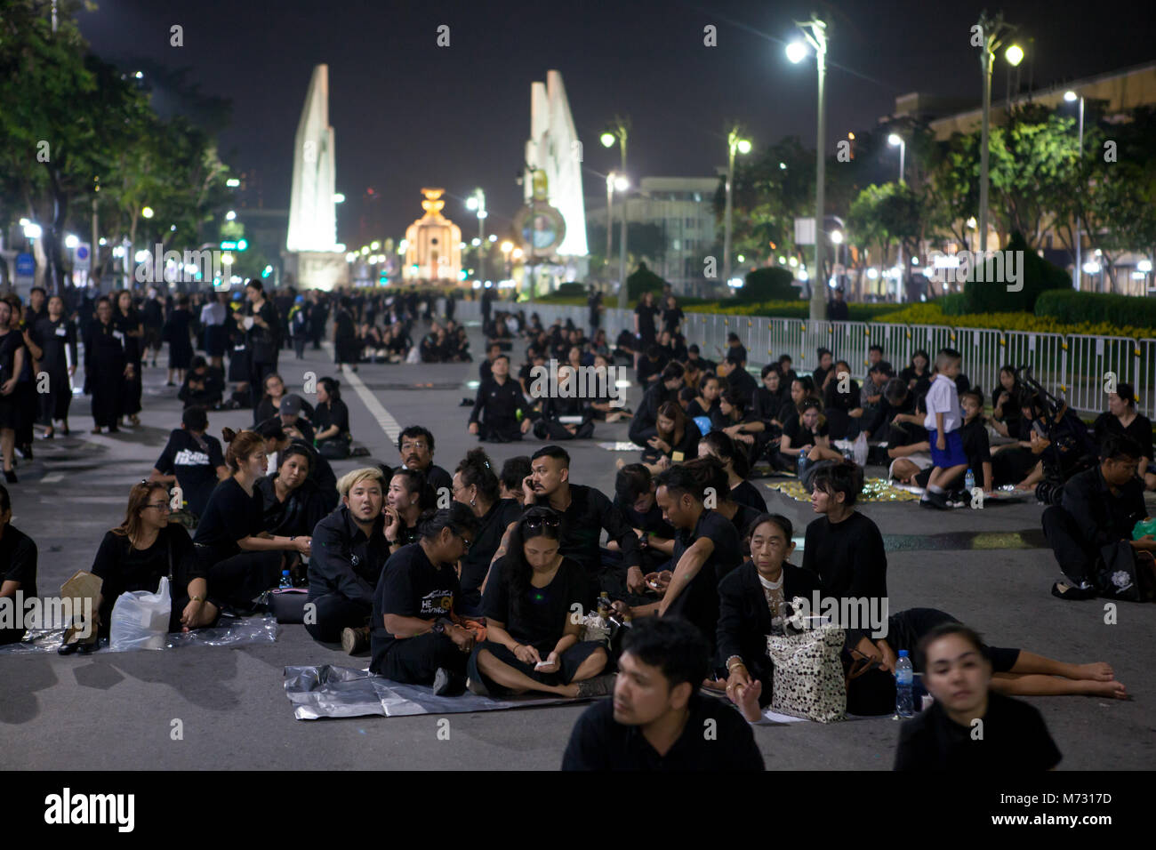 People wearing black clothes sitting in Ratchadamnoen Road after the royal cremation, with the Democracy Monument in the background in Bangkok Stock Photo