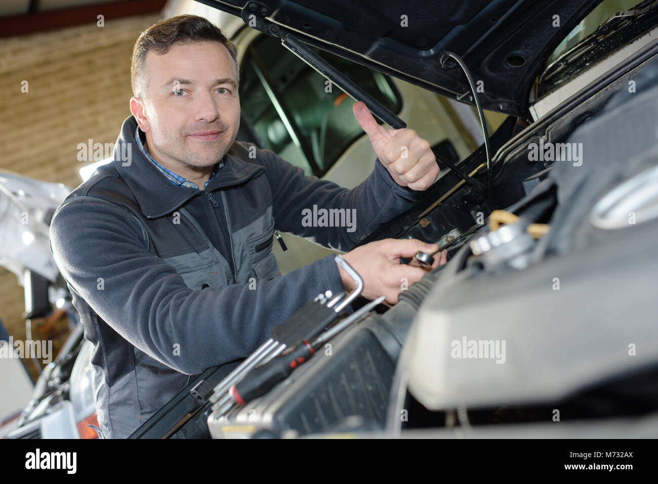 smiling mechanic working on an engines car in a garage Stock Photo - Alamy