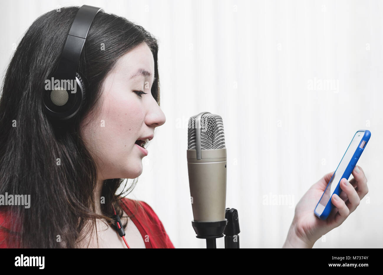Woman singing at a studio microphone, wearing a headphone and reading