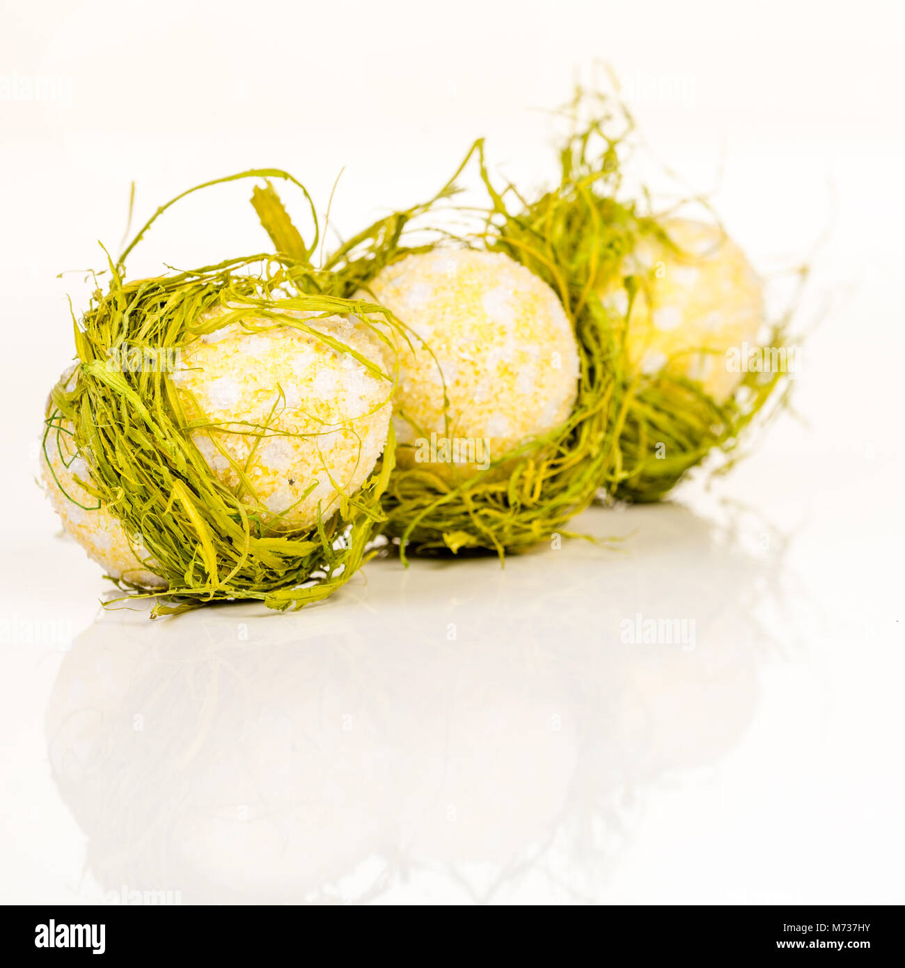 thre Easter egg decoraiton in row wrapped in hay on white Stock Photo