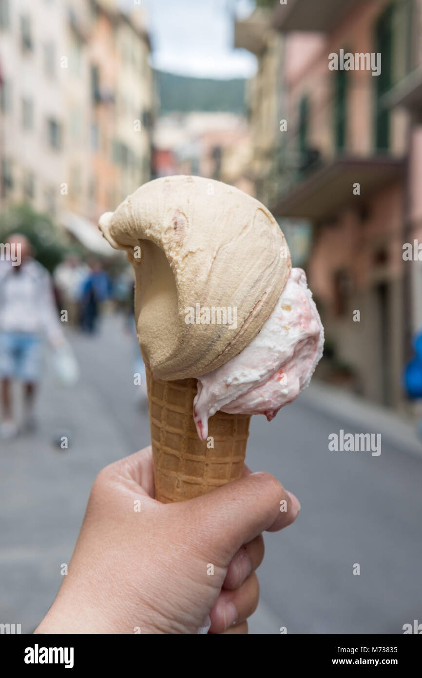 Hand holding Chocolate Gelato, Ice-cream with blur background of a town in Cinque Terre in Italy Stock Photo
