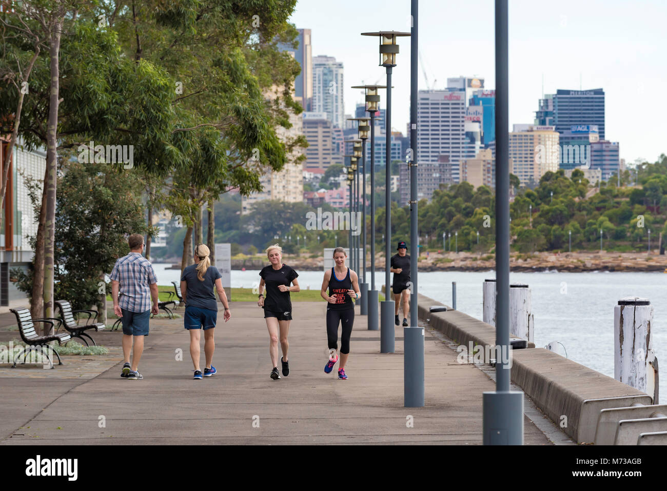 People walking and exercising along a promenade beside Sydney Harbor in Pyrmont, Australia Stock Photo