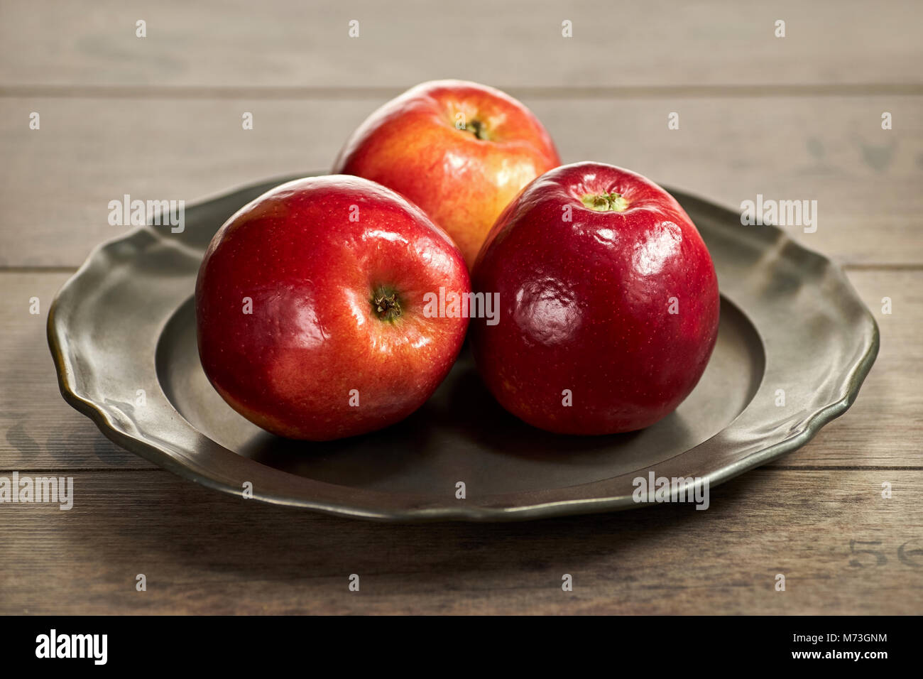 Three red apples on a metal plate Stock Photo