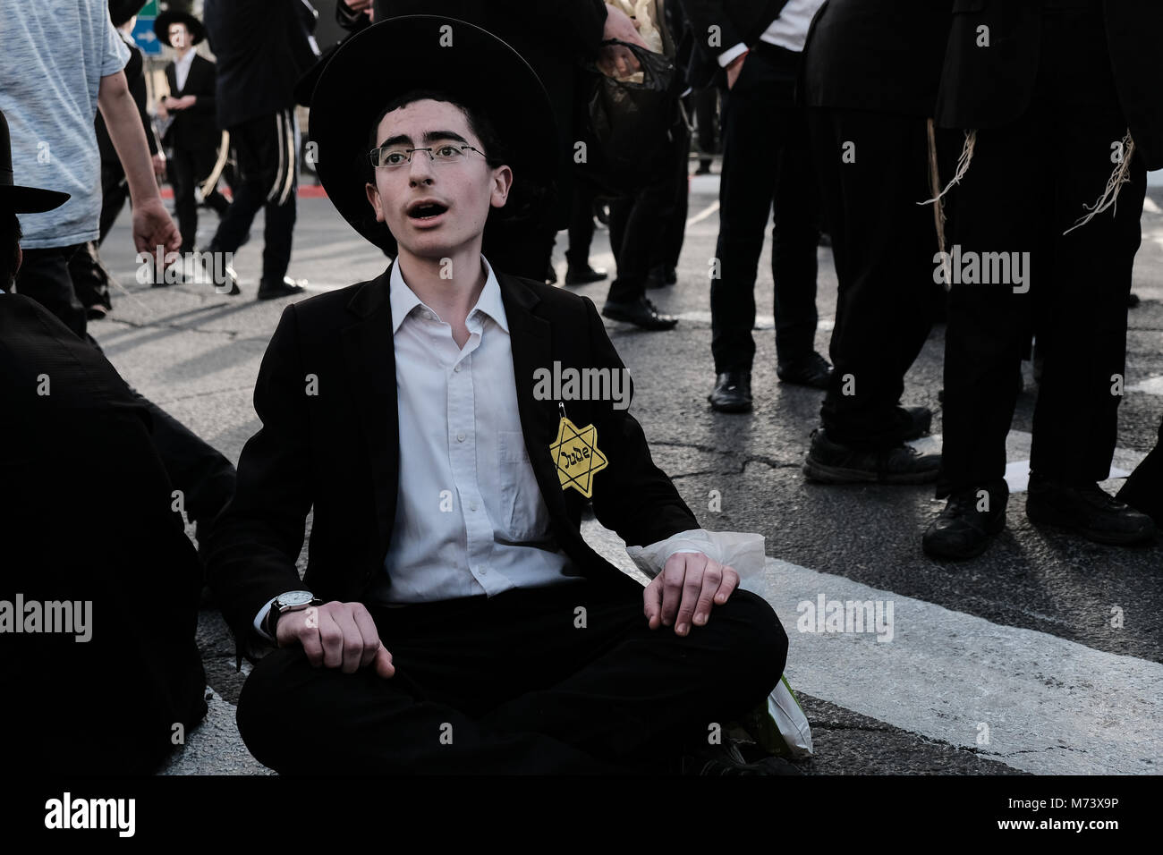 Jerusalem, Israel. 8th March, 2018. A young man wears a yellow Star of David symbolizing Nazi persecution as thousands of ultra-Orthodox Jewish men protest military conscription and the arrest by military police of draft dodgers, blocking the main entrance to Jerusalem, Israel's capital city. In fact, the ultra-Orthodox haredi draft candidates can report to the IDF recruitment office, declare their faith and be exempt from service but some refuse to do so in principal. Credit: Nir Alon/Alamy Live News Stock Photo